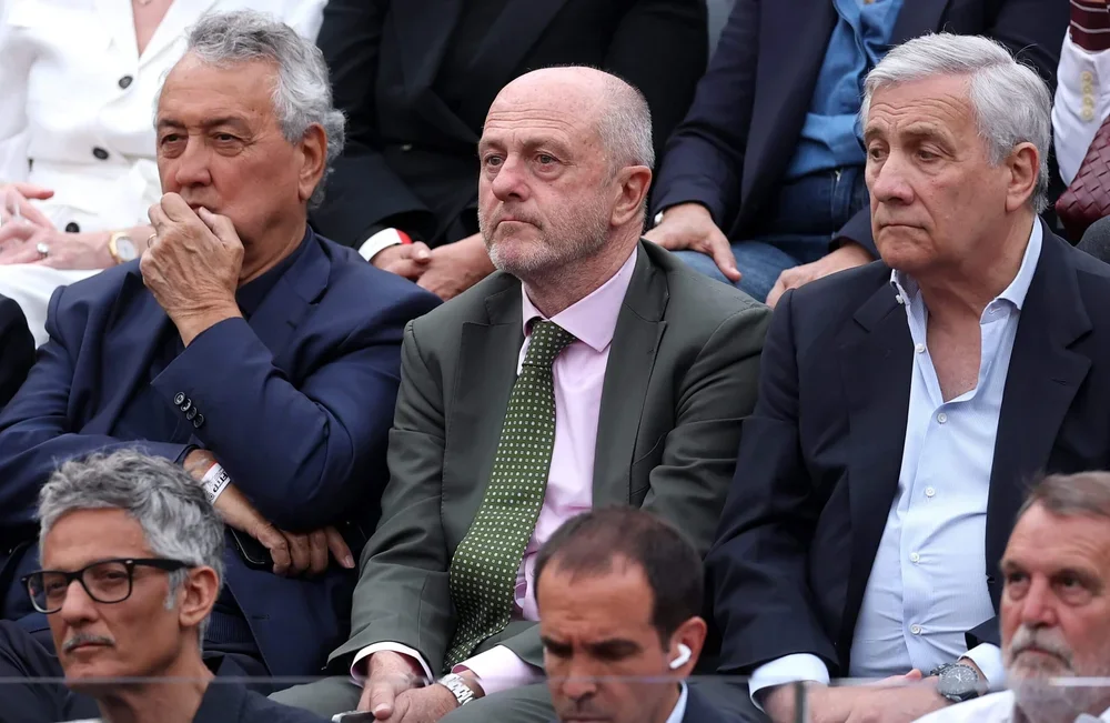 Angelo Binaghi (center) sits in a suit with a green tie between two more men in suits in a sports crowd.